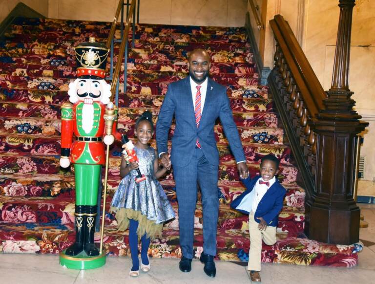 A man holds hands with his children next to a giant Nutcracker statue.