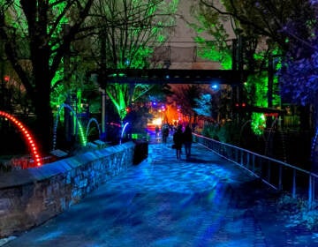 People walk through a lighted pathway at night.