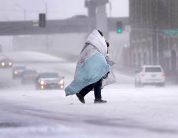 A person wrapped in a blanket crosses a snow-covered street
