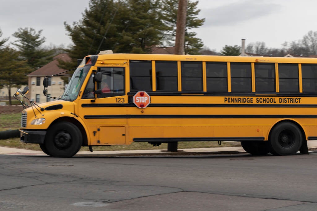 A yellow school bus is driving on a road. The words on the side of the bus read "Pennridge School District."