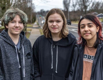 Three people stand shoulder-to-shoulder and pose for a photo. A road is visible in the background.