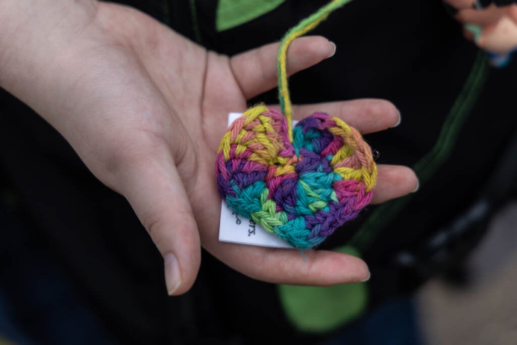 A colorful yarn heart is held in someone's hand.