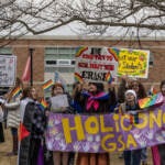 A group of students hold up a sign that reads 