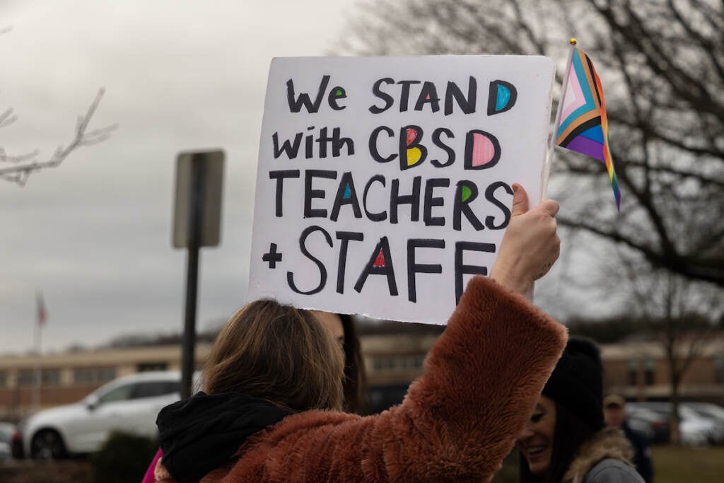 A person holds up a Pride flag.