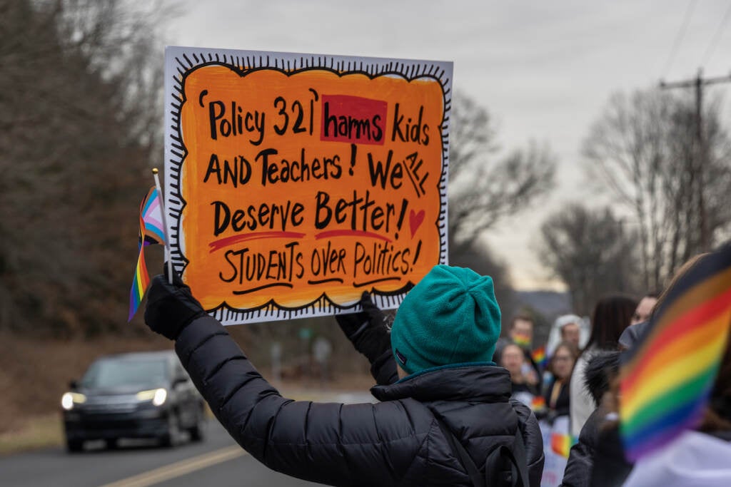 A person holds up a sign decrying Policy 321.