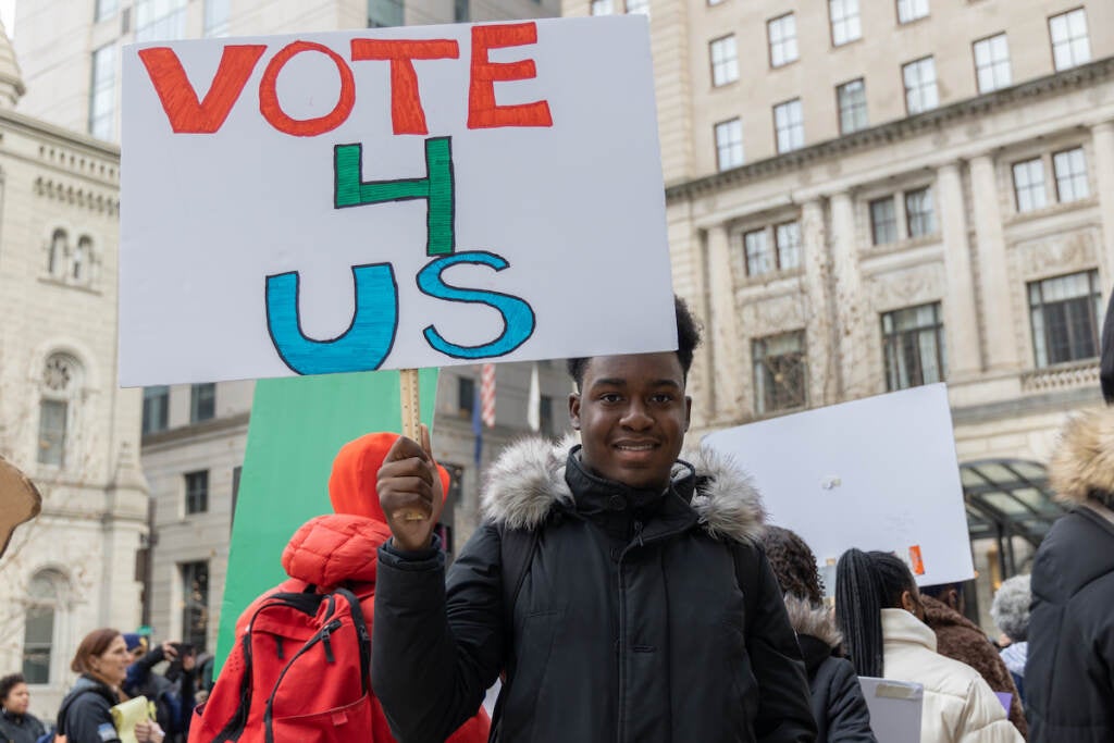 A student holds up a sign that reads "Vote 4 Us."