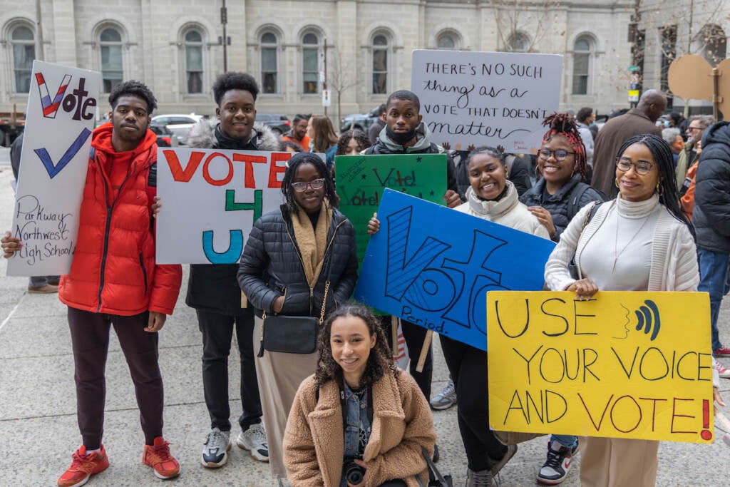 A group of students hold signs that encourage people to vote.