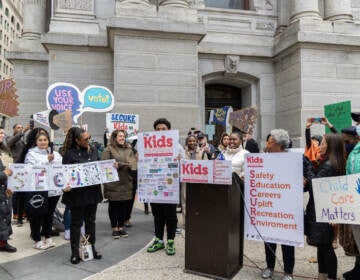 A group of people gather outside of City hall holding signs that reads 