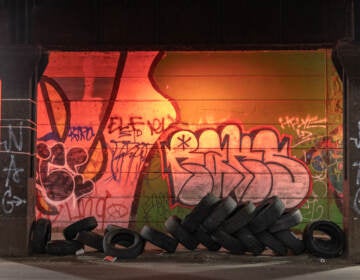 Tires are seen left in an underpass. Graffiti on the wall behind it is visible.