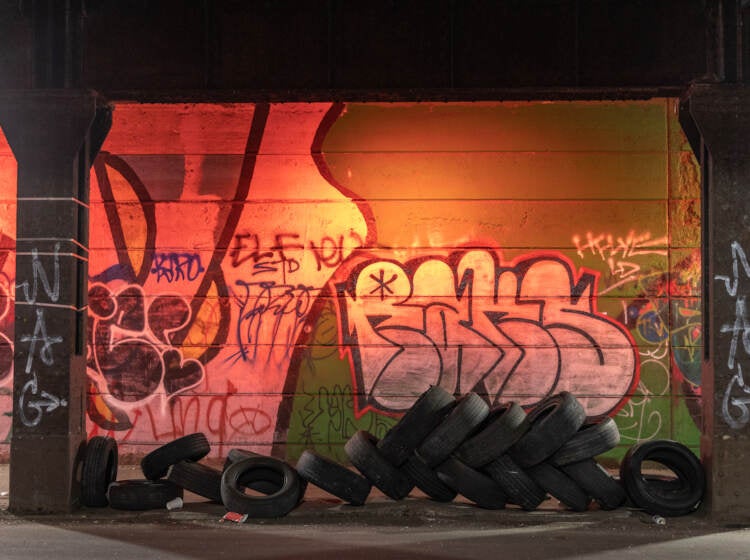 Tires are seen left in an underpass. Graffiti on the wall behind it is visible.