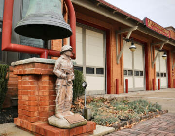 A figurine of a firefighter is in the foreground, and the fire station is in the background.