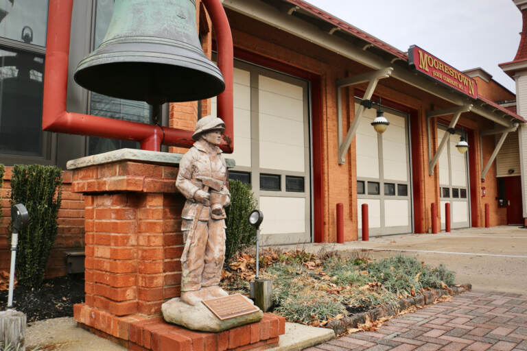 A figurine of a firefighter is in the foreground, and the fire station is in the background.