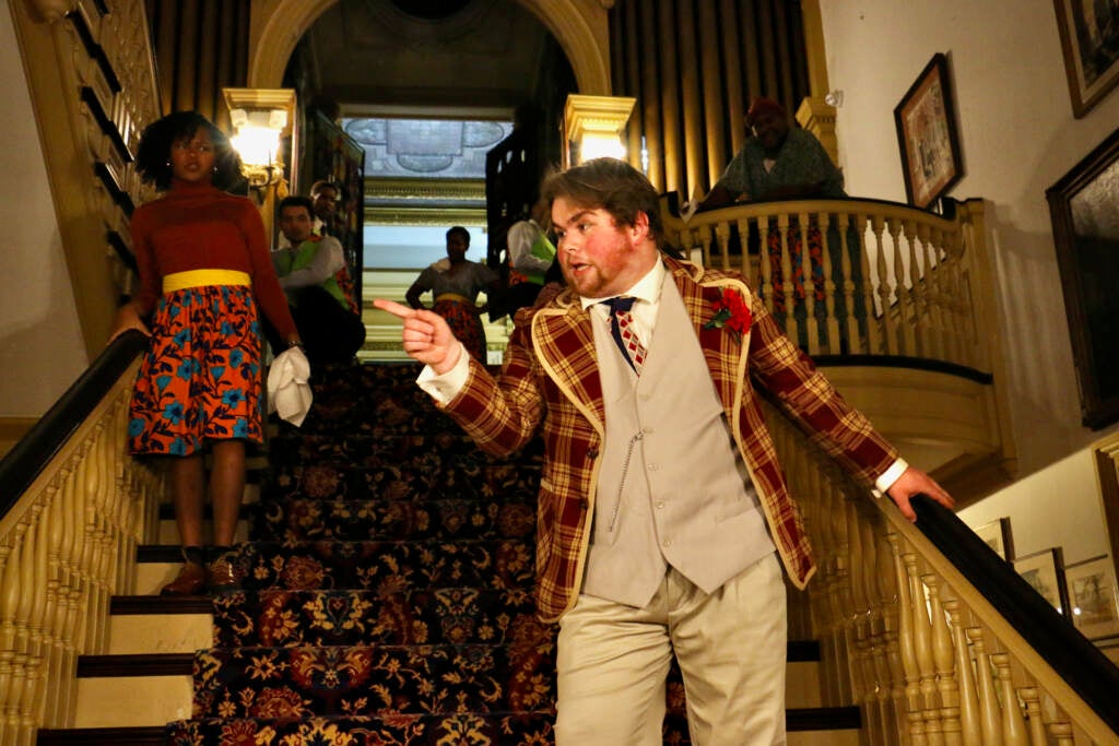 A man stands on a staircase, pointing off camera.