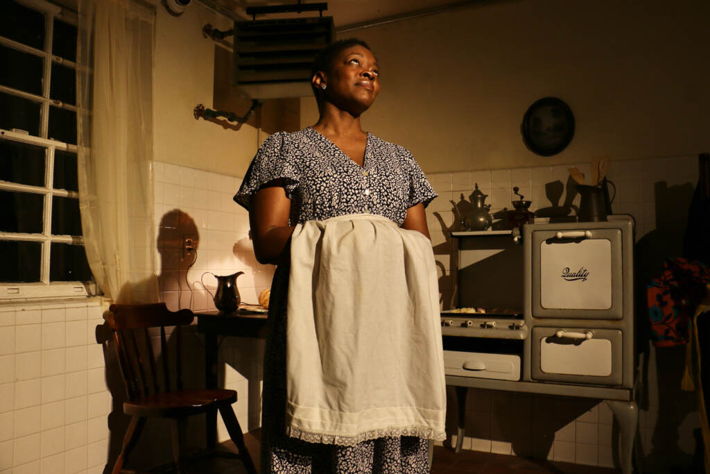 A woman stands with a blanket in her hand, looking upwards.