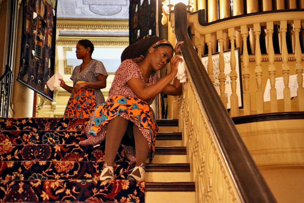 A woman sits on a staircase, dusting the railing.