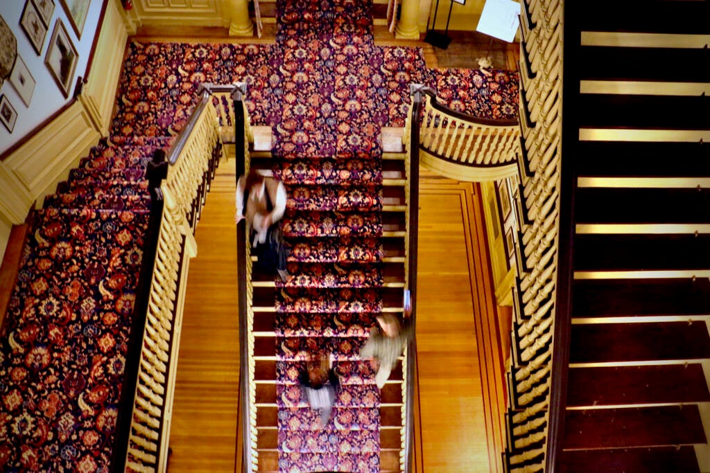 An overhead view of people walking up and down a grand staircase in a mansion.