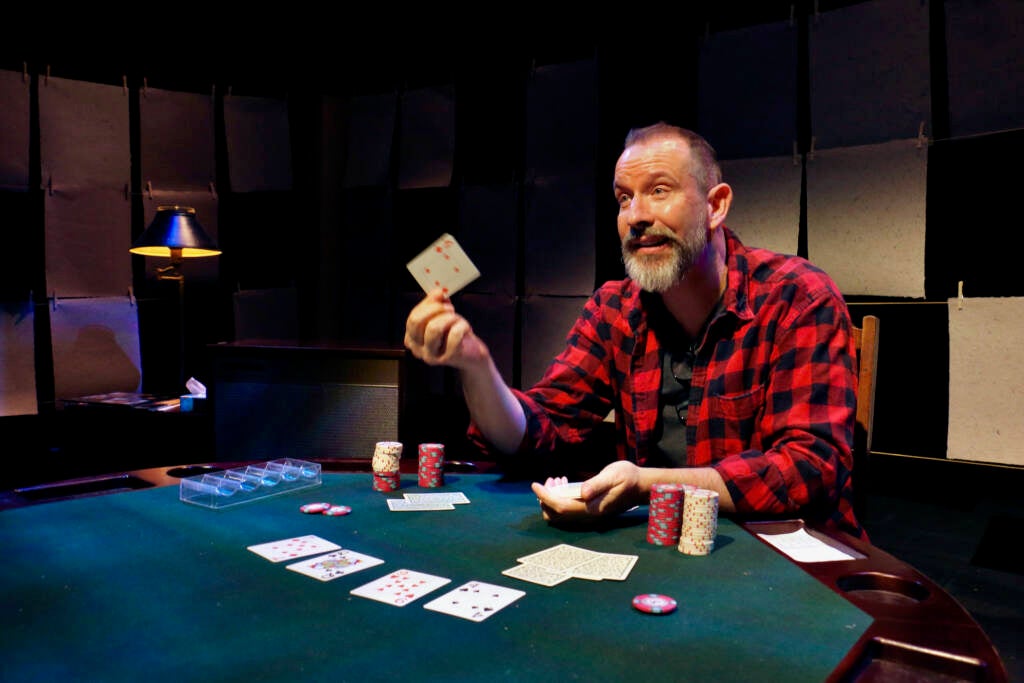 An actor holds up a card while playing poker.