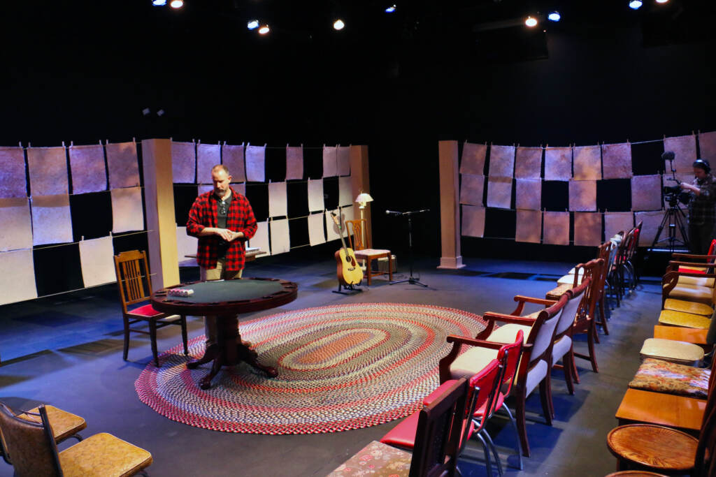 A person stands in the middle of a stage, in front of rows of chairs.