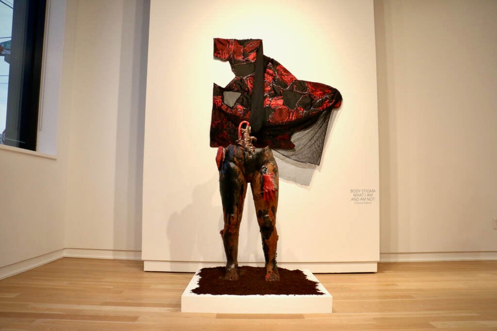 A black and red clothed sculpture visible is displayed in a gallery.