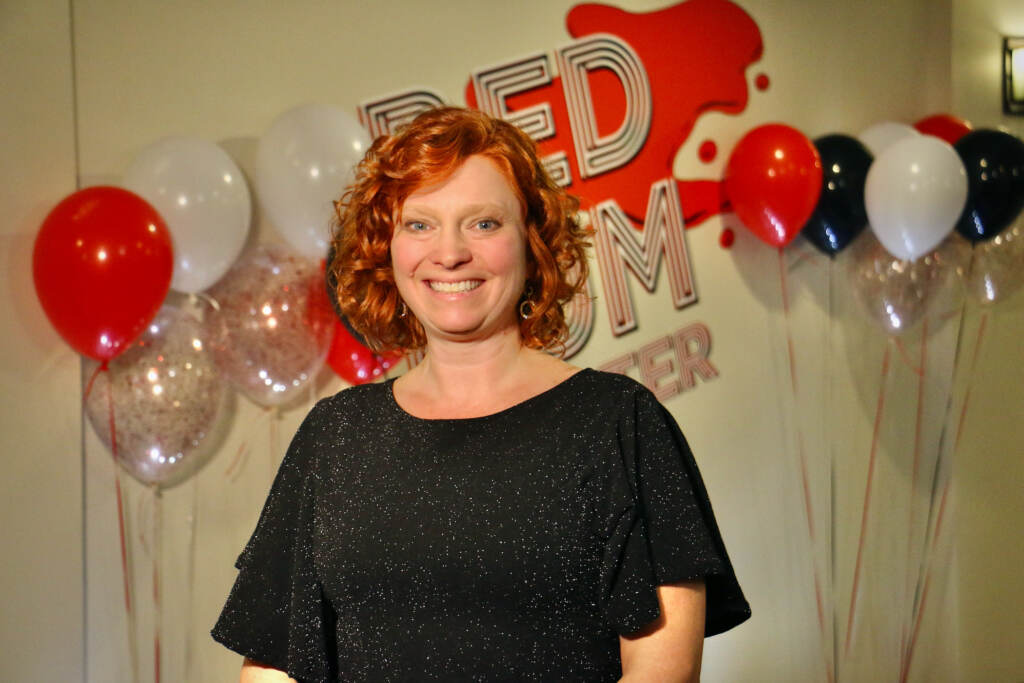 A woman poses for a photo and smiles. There are balloons visible in the background.