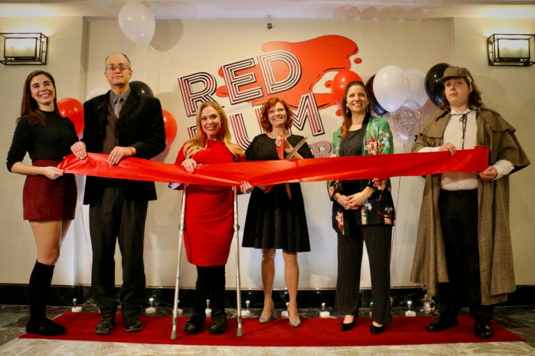 A row of people hold red tape and pose for a photo.