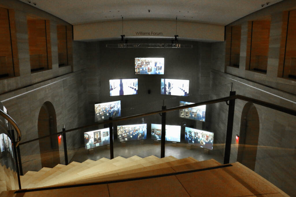 A row of screens are visible in a gallery space below a flight of stairs.