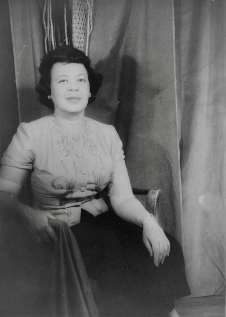 A black-and-white portrait of a woman seated, smiling at the camera.