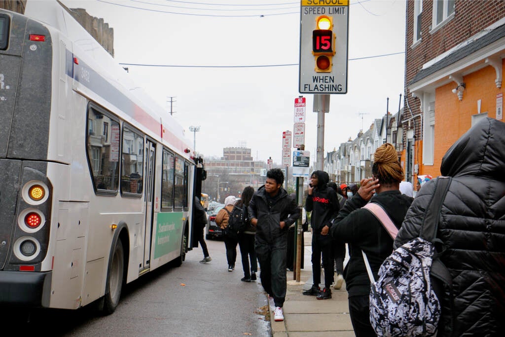 Students wait at a bus stop.