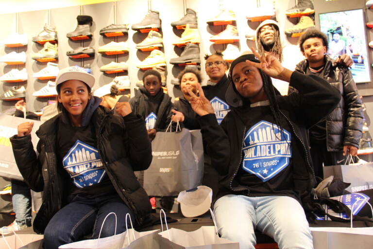 Kids pose for a photo, holding up the peace sign. Sneakers are visible in the background.