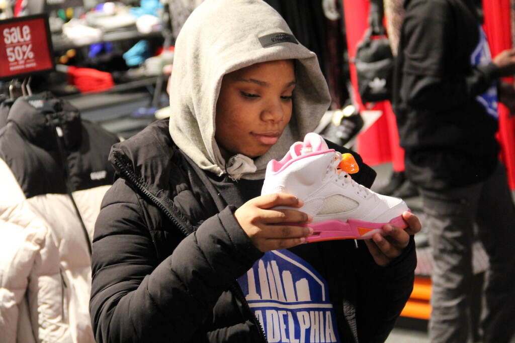 A kid stares at a pink and white basketball shoe they are holding in front of them.
