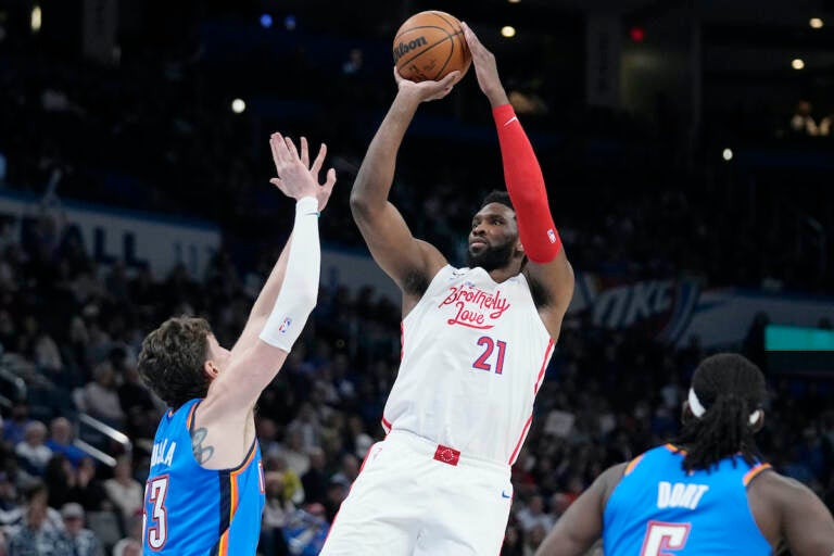 Philadelphia 76ers center Joel Embiid (21) shoots between Oklahoma City Thunder center Mike Muscala, left, and guard Luguentz Dort, right, in the first half of an NBA basketball game Saturday, Dec. 31, 2022, in Oklahoma City. (AP Photo/Sue Ogrocki)