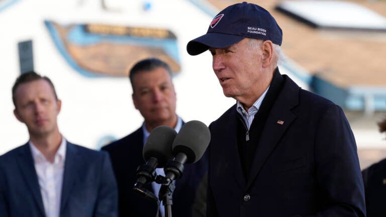 Biden, wearing a baseball cap, speaks into a microphone.