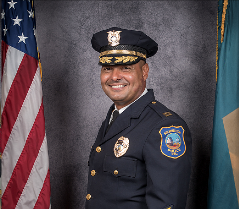 Wilfredo Campos poses in police uniform in front of a U.S. flag.