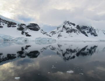 A snowcapped landscape is reflected in a body of water.