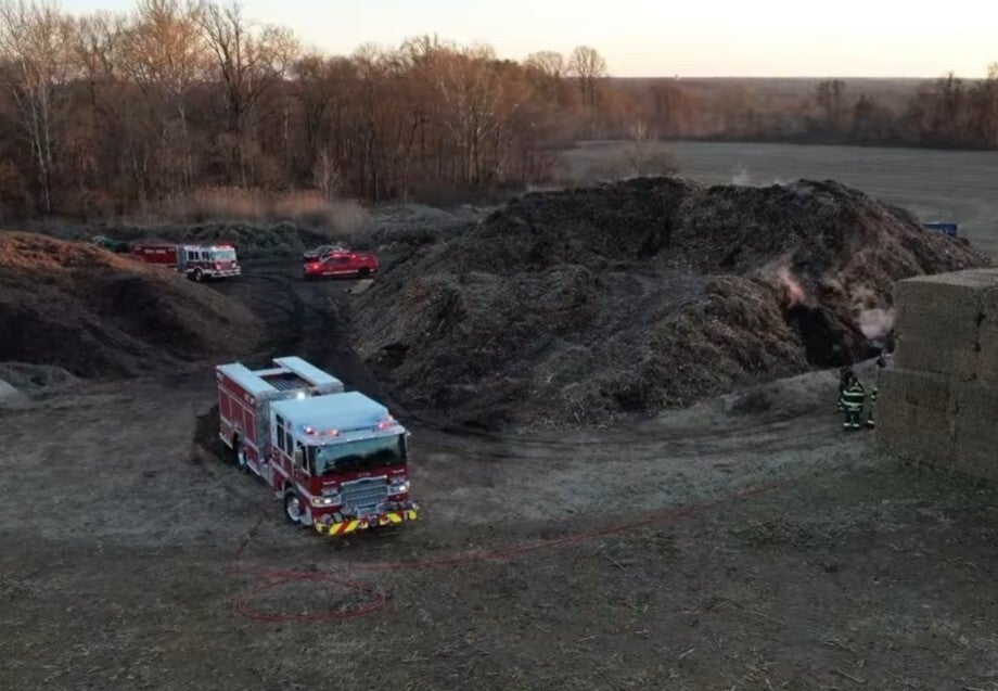 A firetruck is parked next to a fire in a dump site.