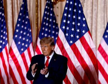 Donald Trump claps in front of a row of American flags.