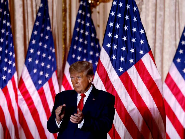 Donald Trump claps in front of a row of American flags.