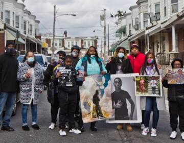 A group of people stand together in the middle of a street holding photographs.