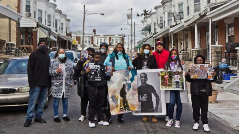 A group of people stand together in the middle of a street holding photographs.