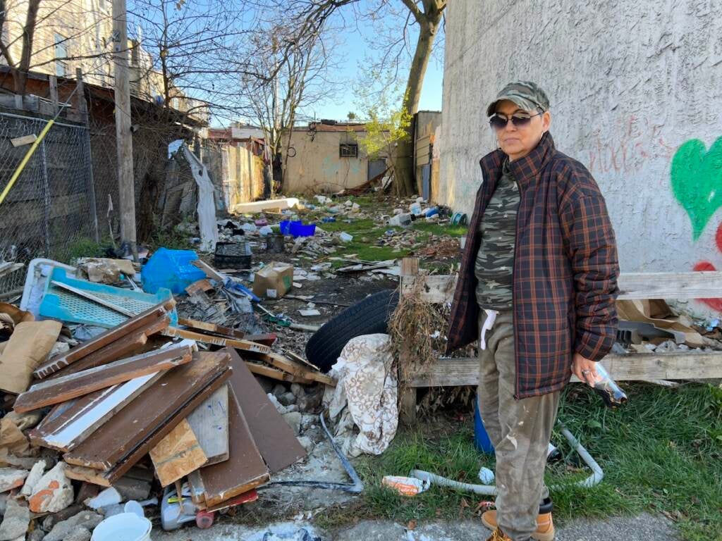 Marilyn Rodriguez stands in a vacant lot. A pile of debris is