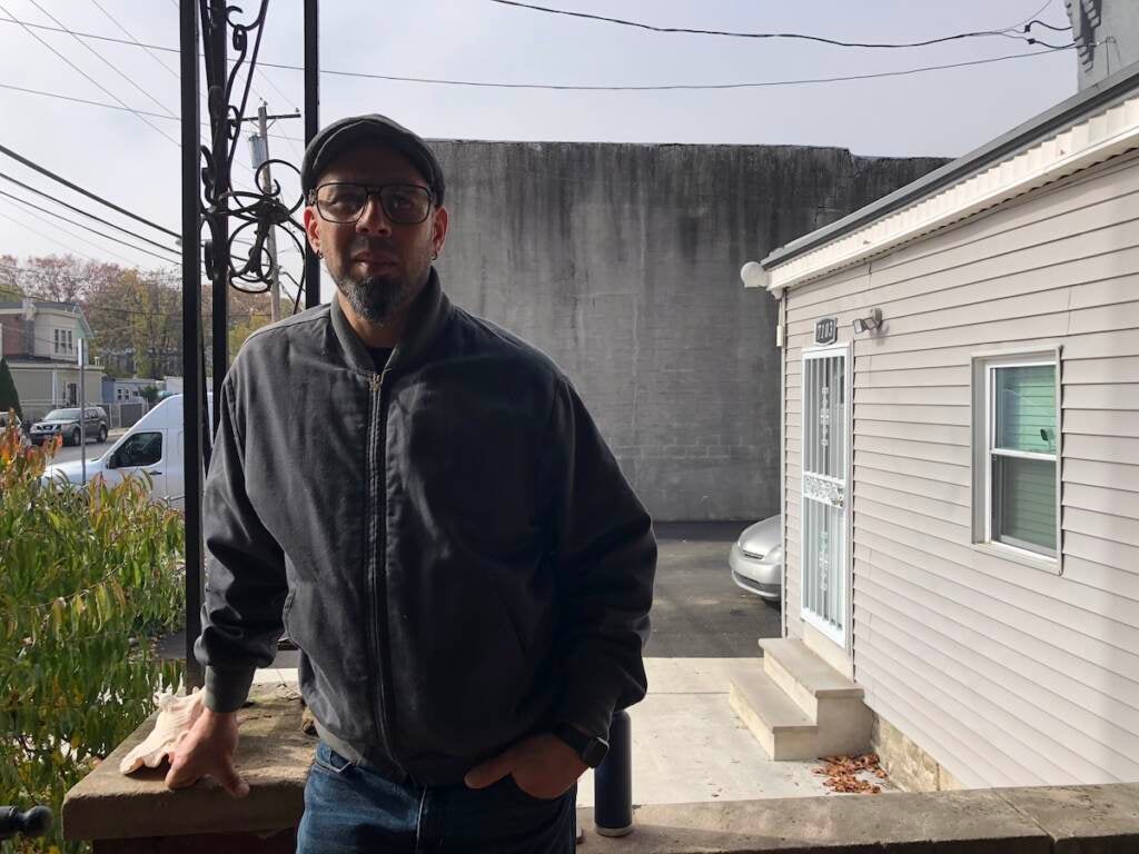 A man leans on a railing. Houses are visible in the background.