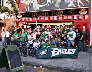 A group of people pose in front of a pub with a big Eagles banner.