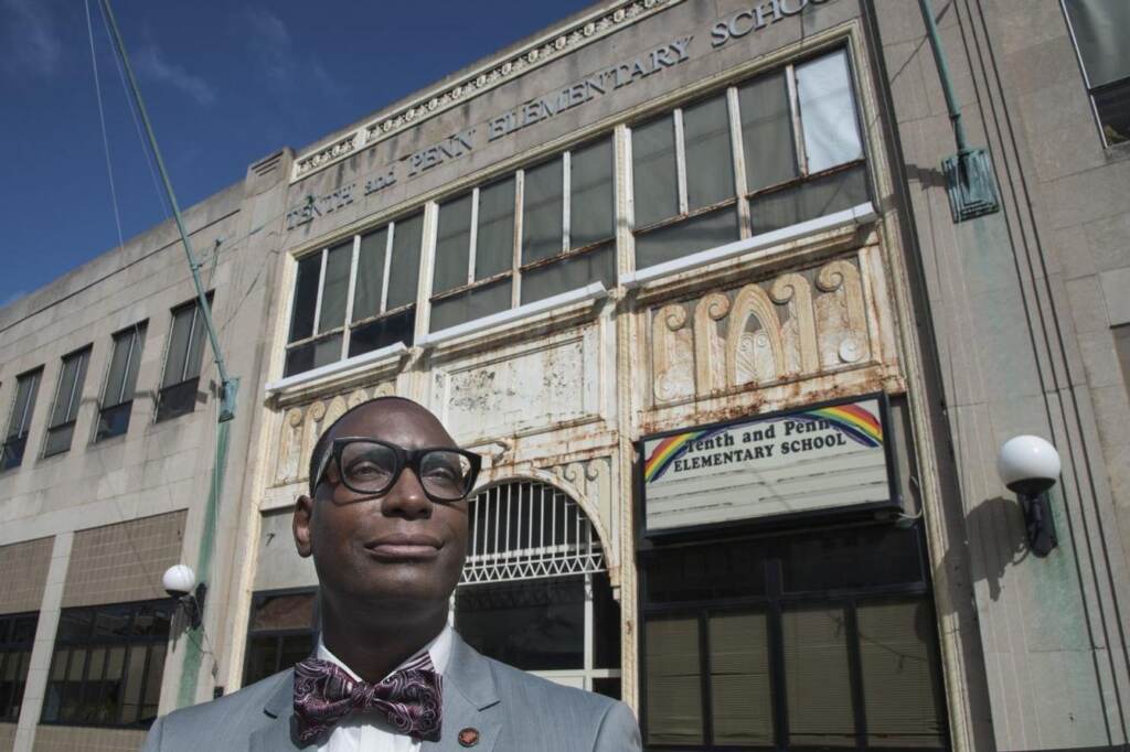 A man smiles as he stands in front of a school building.