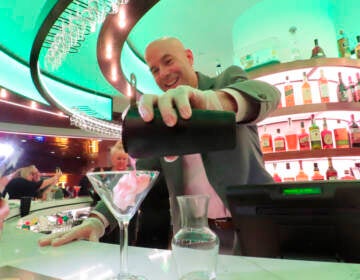 A bartender pours a drink into a martini glass at a bar.