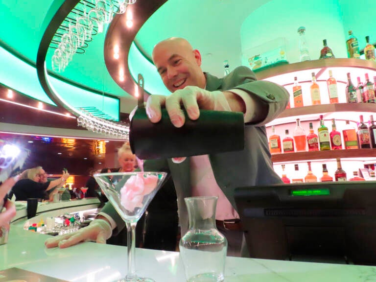 A bartender pours a drink into a martini glass at a bar.