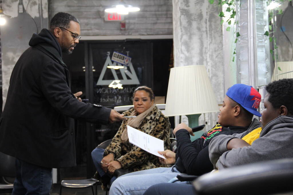 A person hands out sheets of paper to a group of people who are seated.