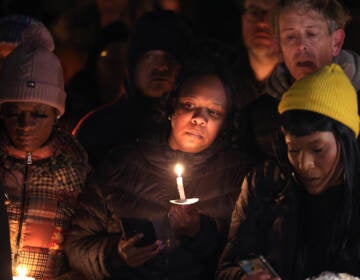 A candle lits a person's face in a group of mourners.