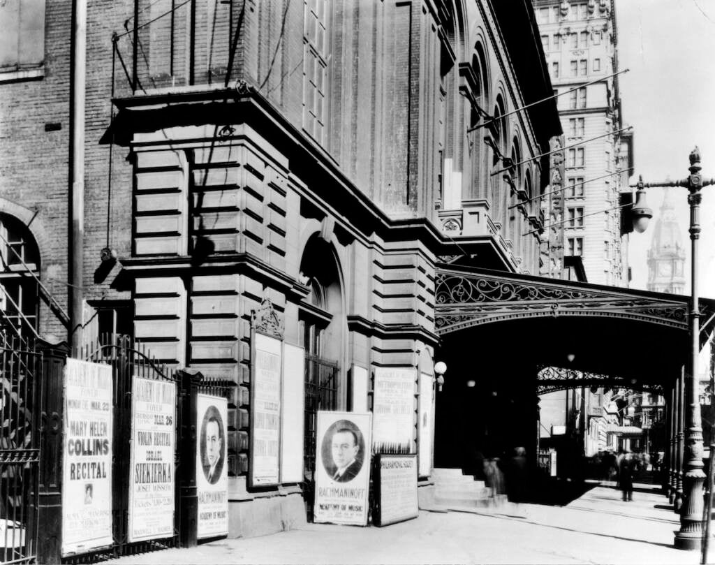 A black-and-white photo shows posters advertising a concert outside of a building