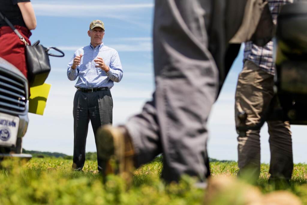 A man stands in a field talking to a group of people.