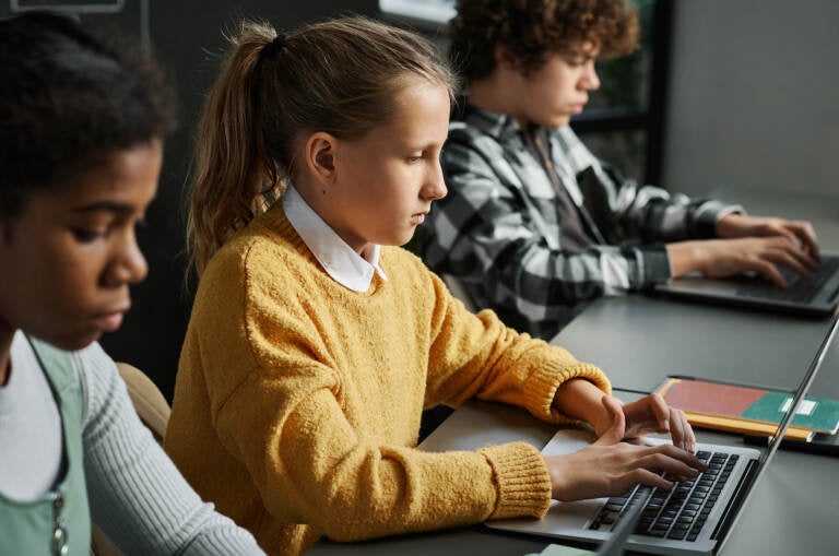 Three students seated at a table look at laptops.